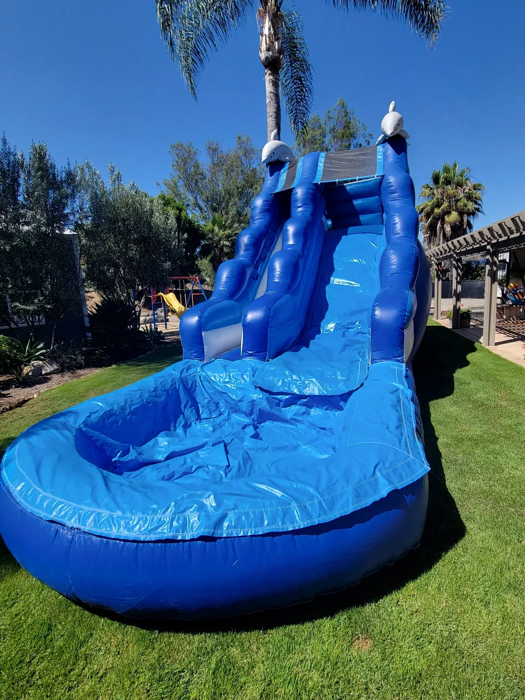 A blue inflatable water slide in the middle of a yard.