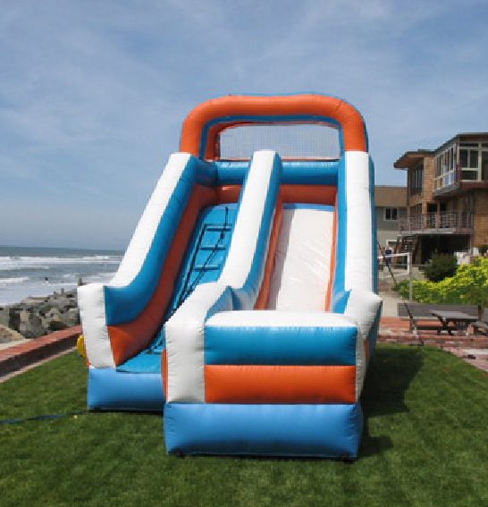 A large inflatable slide in the grass near the beach.