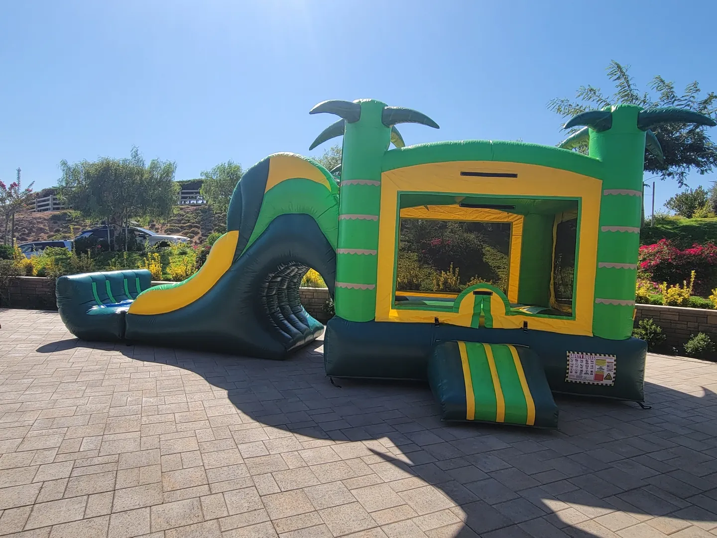 A green and yellow inflatable slide with palm trees.