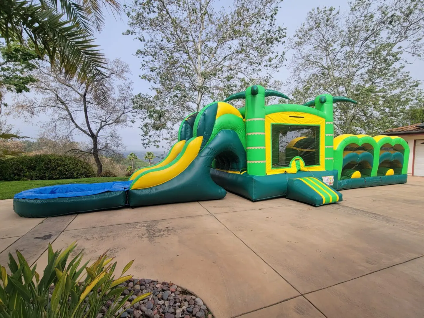 A green and yellow inflatable slide in the middle of a driveway.